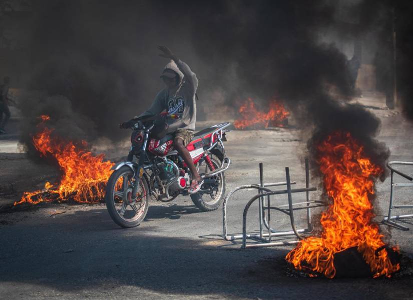 Una persona se transporta en motocicleta con incendios alrededor, este viernes en Puerto Príncipe (Haití). EFE/Johnson Sabin