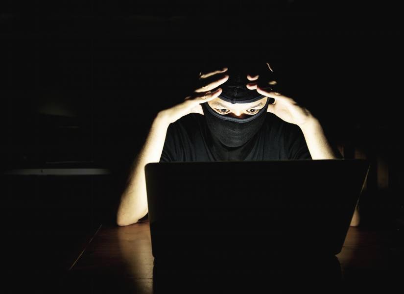 Hacker cubierto la cara en un cuarto oscuro.