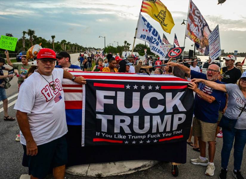 Manifestantes sostienen carteles y banderas, y jalan un ataúd envuelto en una bandera estadounidense, cerca de la residencia en Mar-a-Lago del presidente estadounidense Donald Trump.