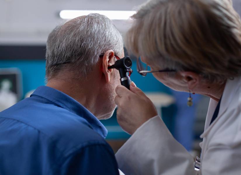 Una doctora utiliza un otoscopio para realizar una consulta de oído a un anciano durante su cita médica.