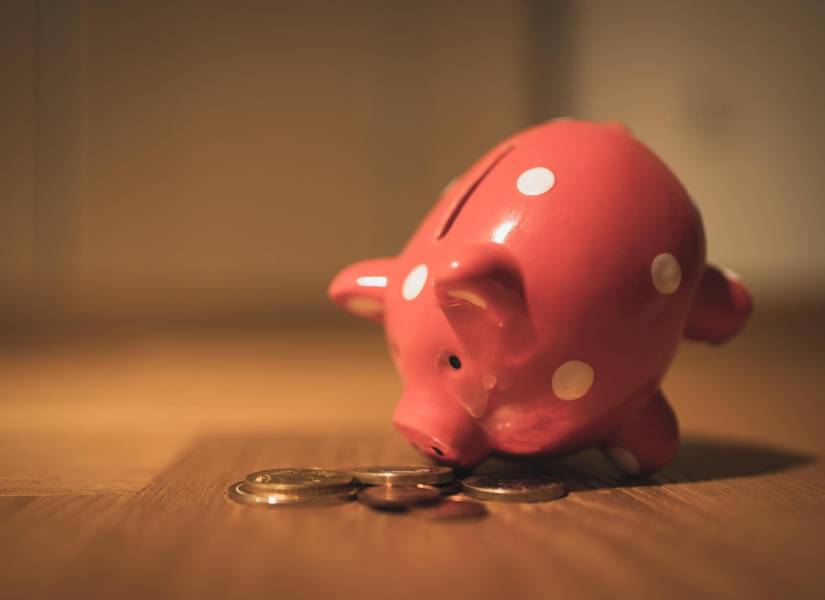 Imagen de una alcancía de ahorro con forma de chancho, con monedas afuera.