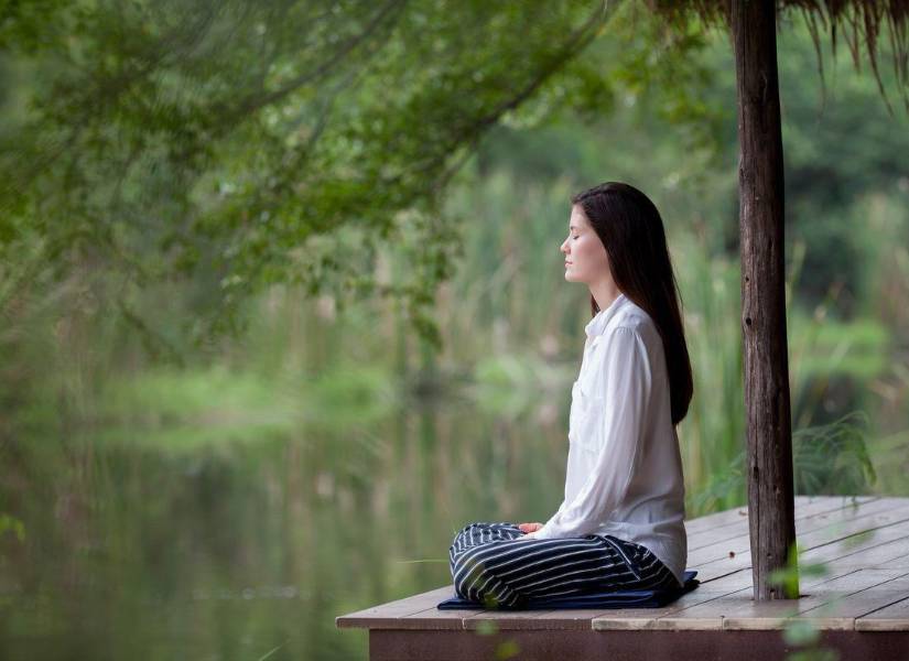 Imagen descriptiva de una mujer sentada meditando en la naturaleza.