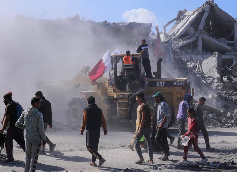 Palestinos camina al lado de un bulldozer desplegado por el Municipio de Gaza para limpiar las calles