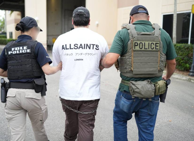 Fotografía cedida por el Departamento de Aplicación de la Ley de Florida (FDLE) de agentes de la policía trasladando a un inmigrante detenido durante la operación Marea Negra este jueves, en Miami (Estados Unidos).