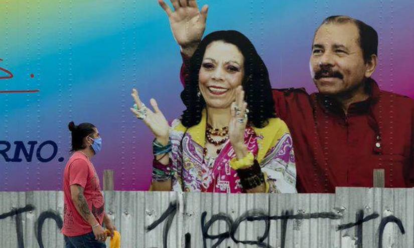 Una persona camina por una calle con la imagen de Daniel Ortega y la vicepresidenta Rosario Murillo de fondo.